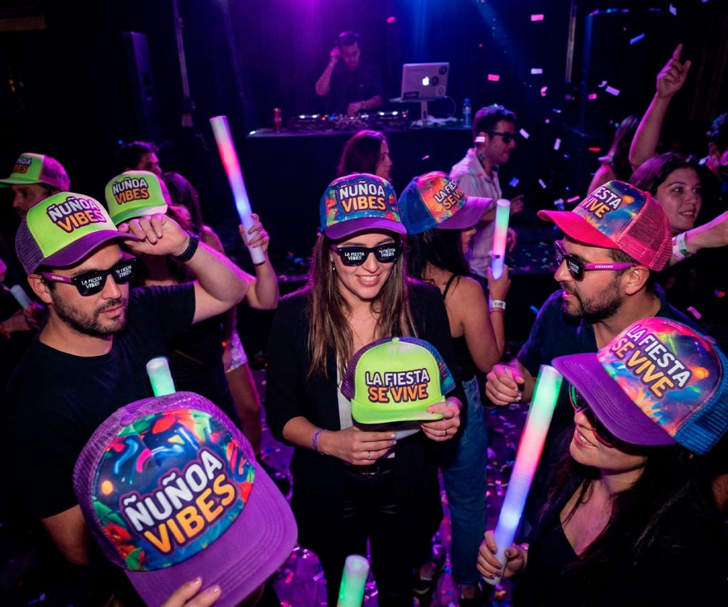 Grupo de amigos celebrando con cotillón premium personalizado: gorros de espuma y lentes vibrantes en Ñuñoa